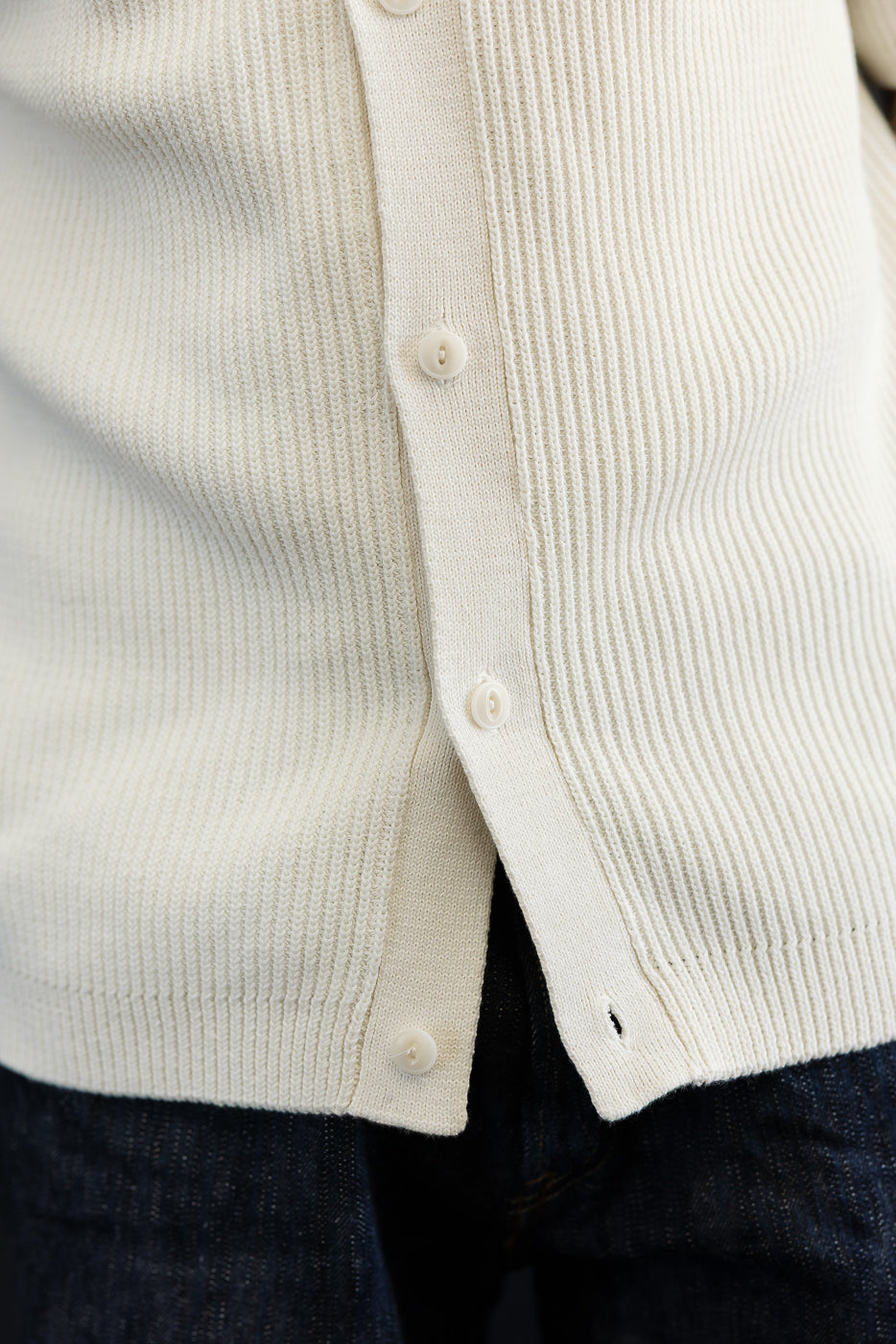Close-up of front hem and buttons on ribbed cotton knit short sleeve shirt in natural color.