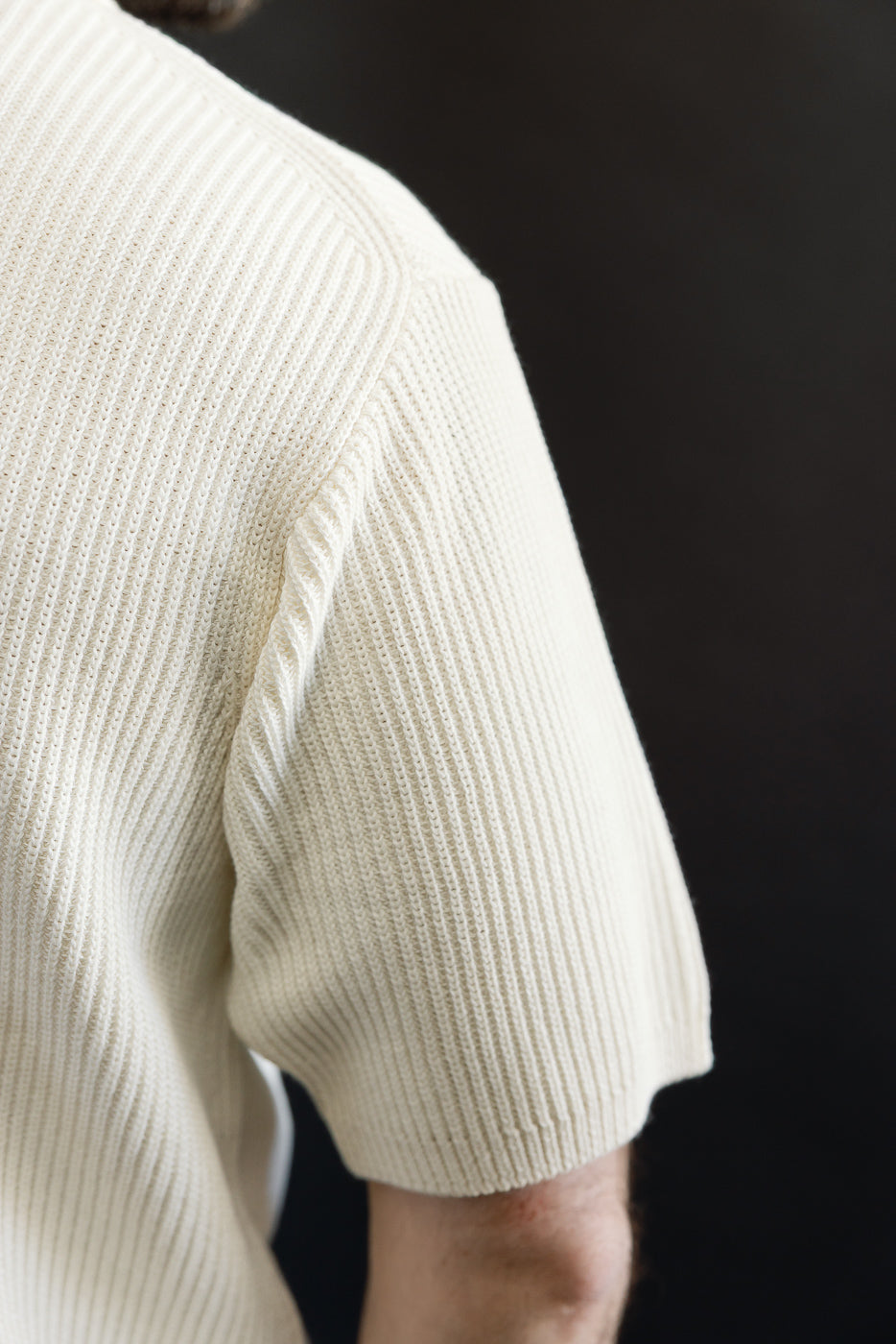 Close-up of male model's upper arm wearing ribbed cotton knit short sleeve shirt, right side view, showing fabric texture; model is 5'9