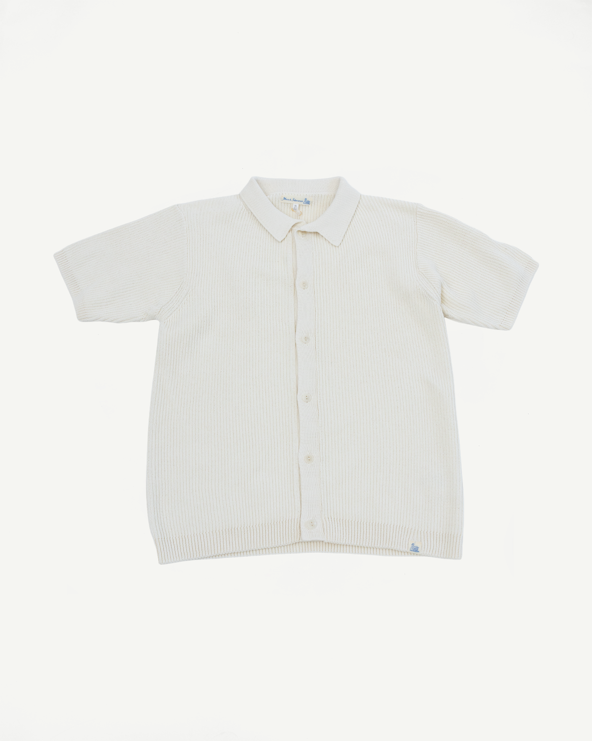 Flat lay of front of ribbed cotton knit short sleeve shirt in natural color, showing buttons, collar, and hem detail.