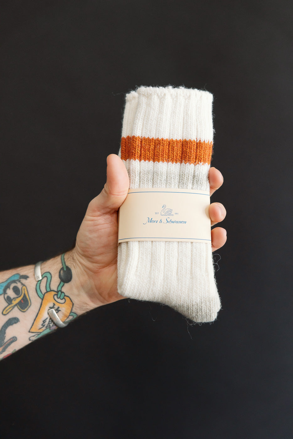 Close-up of hand holding Merz b. Schwanen recycled wool socks, front side with amber stripe detail.