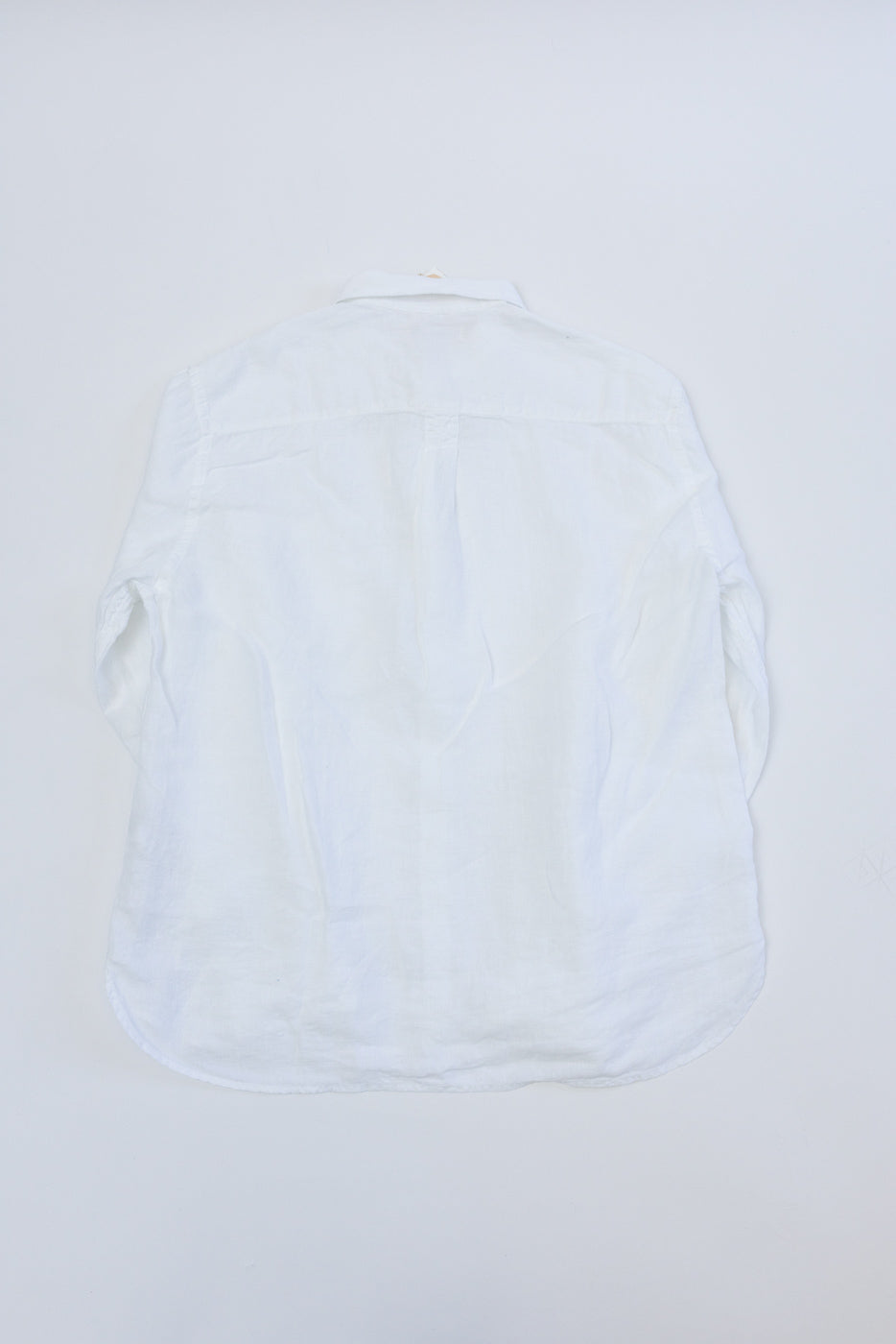 Flat lay of organic linen long sleeve shirt in white, back view, curved hem detail visible.