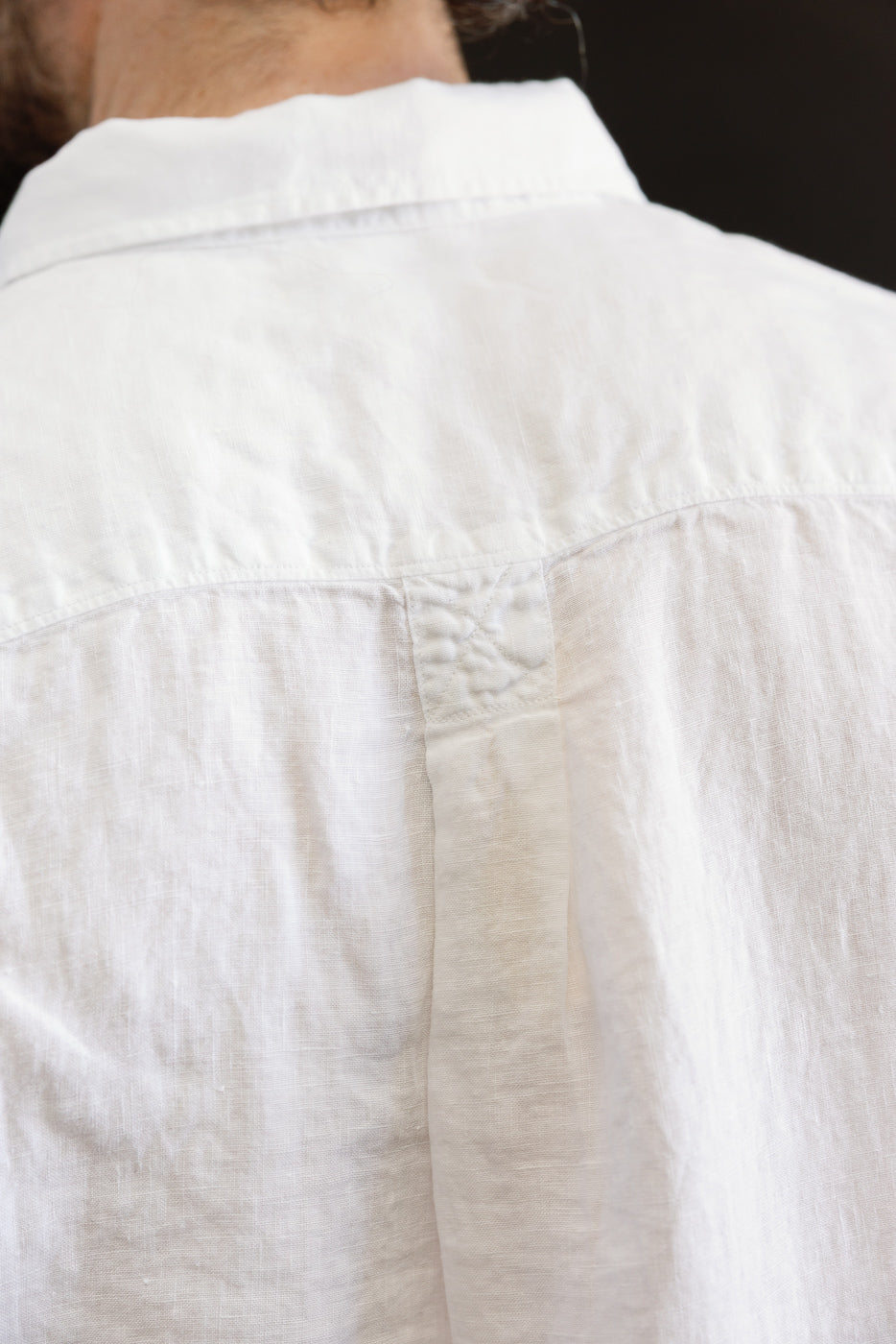 Close-up of the back upper panel and collar detail on a white organic linen men's long sleeve shirt, showing fabric texture and stitching on male model, 5'9