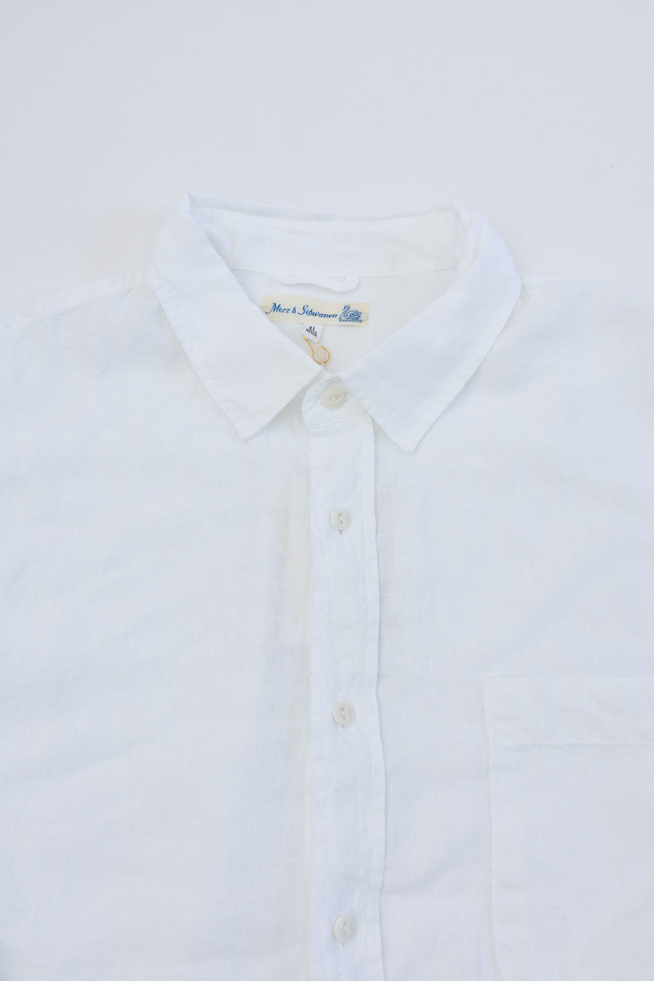 Close-up of front collar, buttons, and pocket on white long sleeve organic linen shirt.