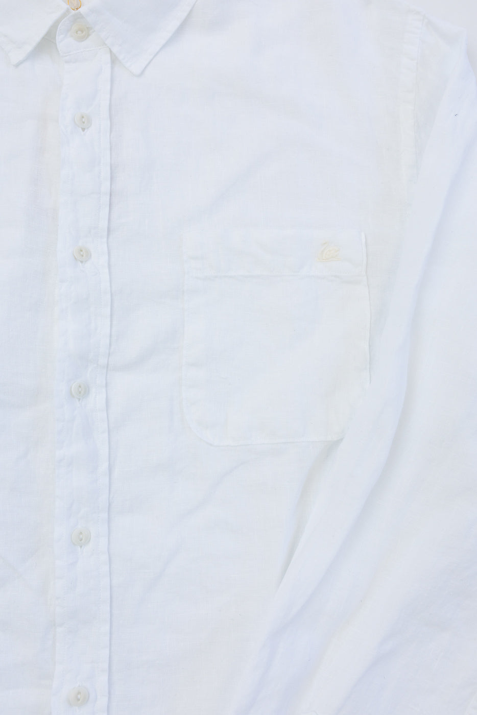 Close-up front view of white organic linen long sleeve shirt chest pocket, showing buttons, collar, and fabric texture.
