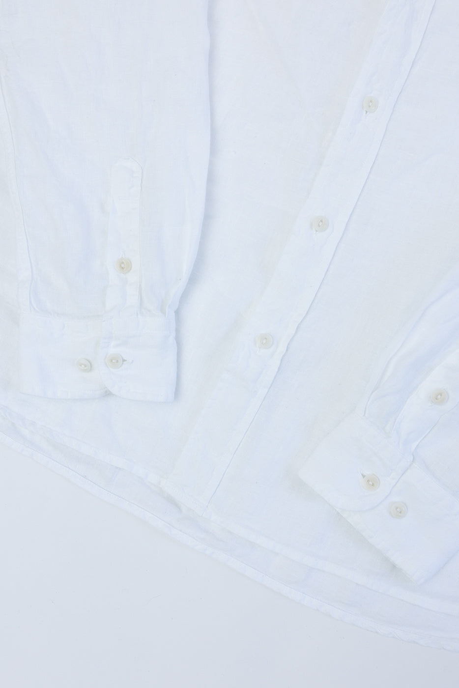 Close-up of front lower section of white organic linen long sleeve shirt showing cuffs, buttons, and curved hem.