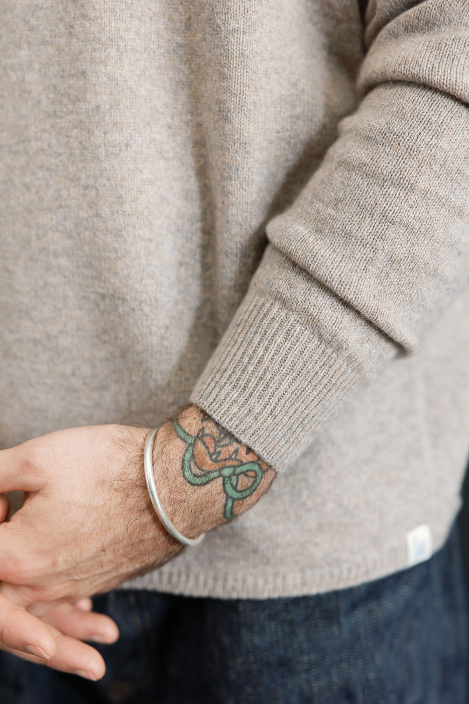 Close-up of the left sleeve and ribbed cuff of a tan knit sweater on a male model.