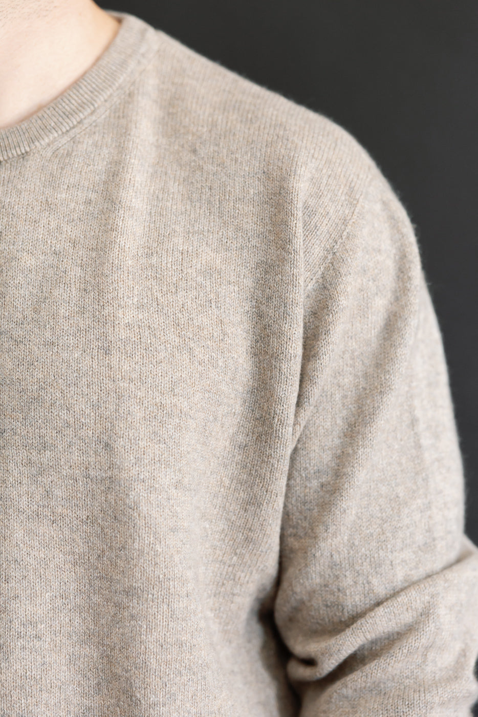 Close-up of the front texture and crew neck of a beige knit sweater.