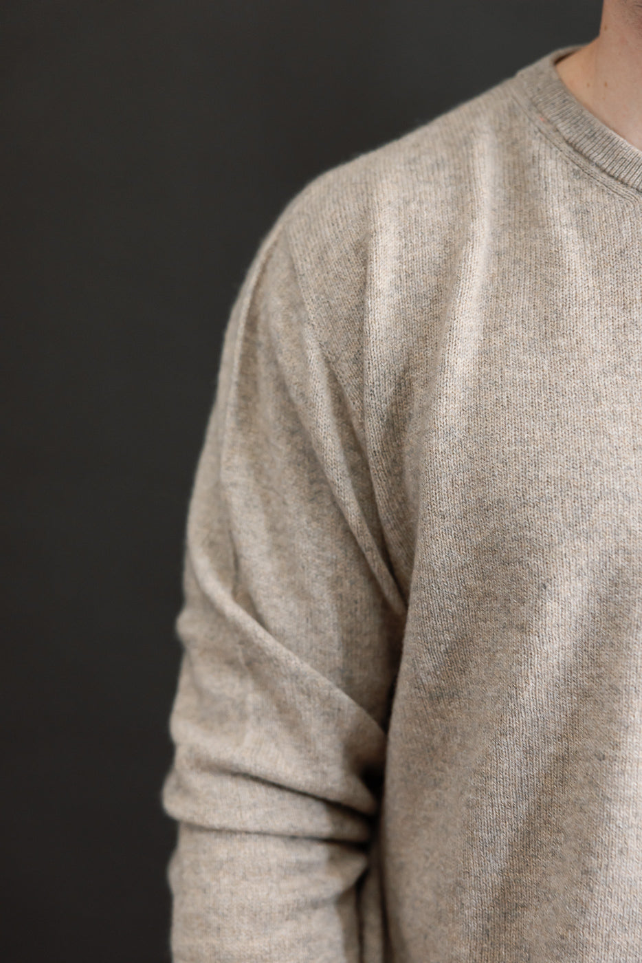 Close-up of the right side and sleeve of a beige knit sweater on a male model, 5'9
