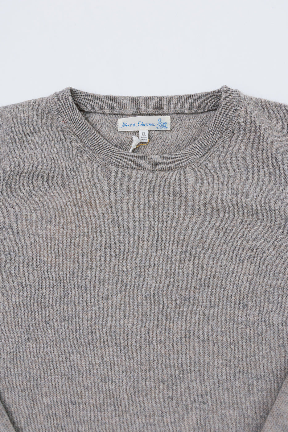 Close-up front view of a grey knit sweater showing the ribbed crewneck and brand tag.