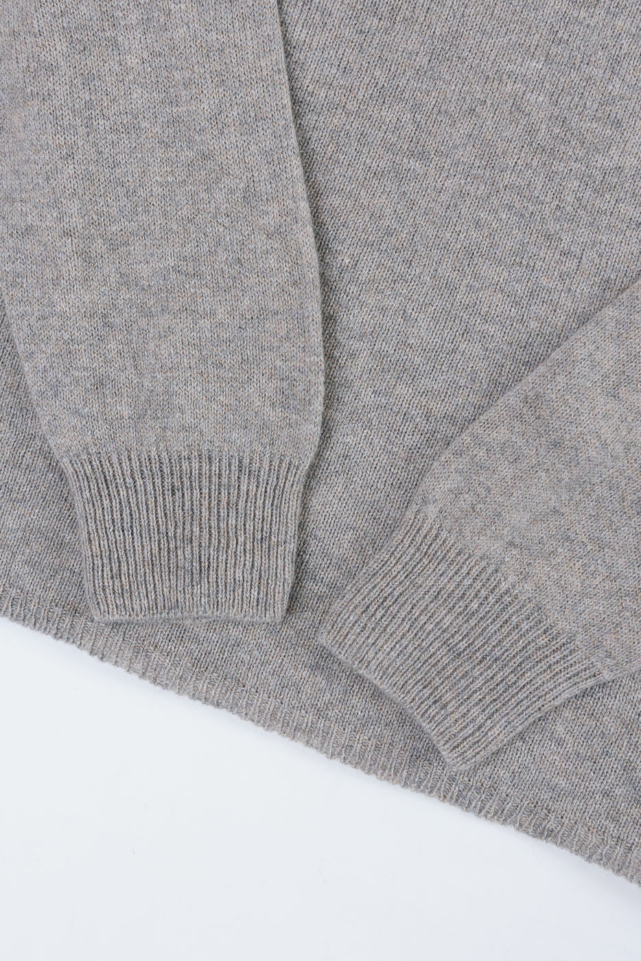 Close-up of the ribbed cuffs and textured grey knit fabric of a sweater.