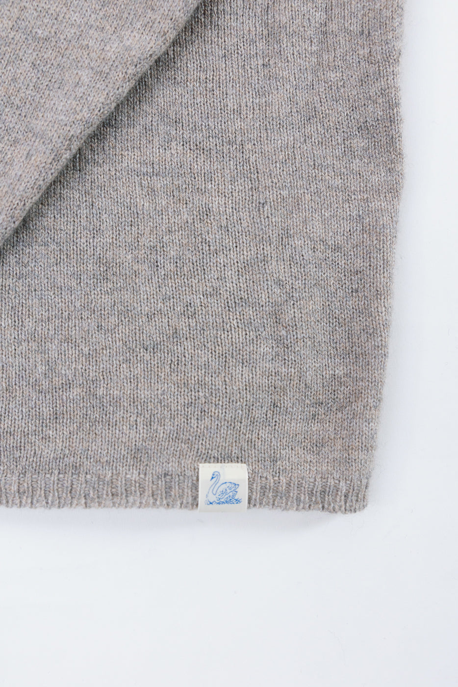 Close-up of a grey knit sweater's bottom hem and fabric texture with a swan brand tag.