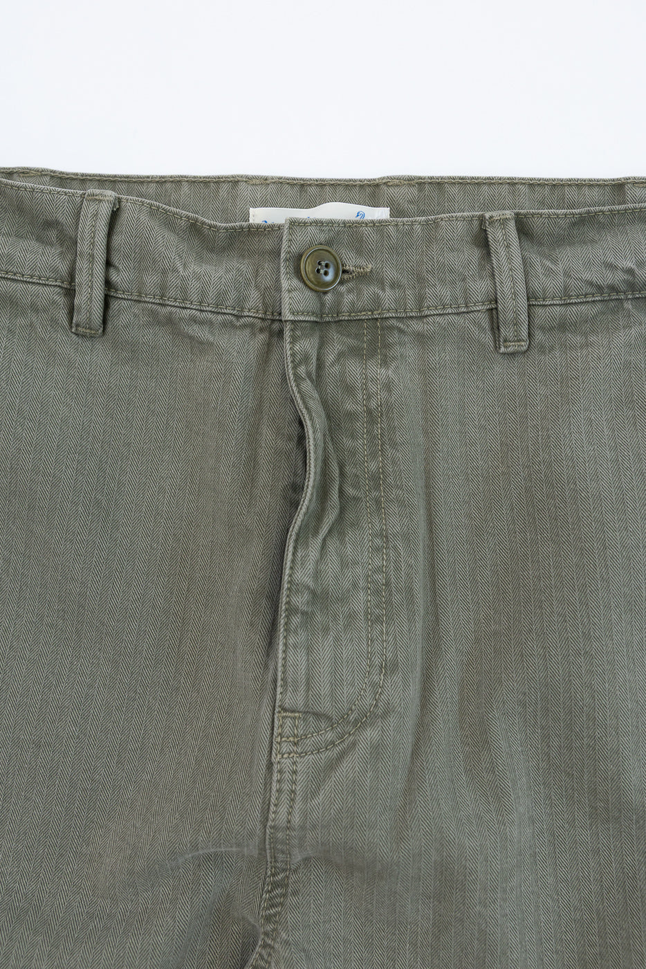 Close-up of the front waist and button closure of olive green herringbone twill trousers.