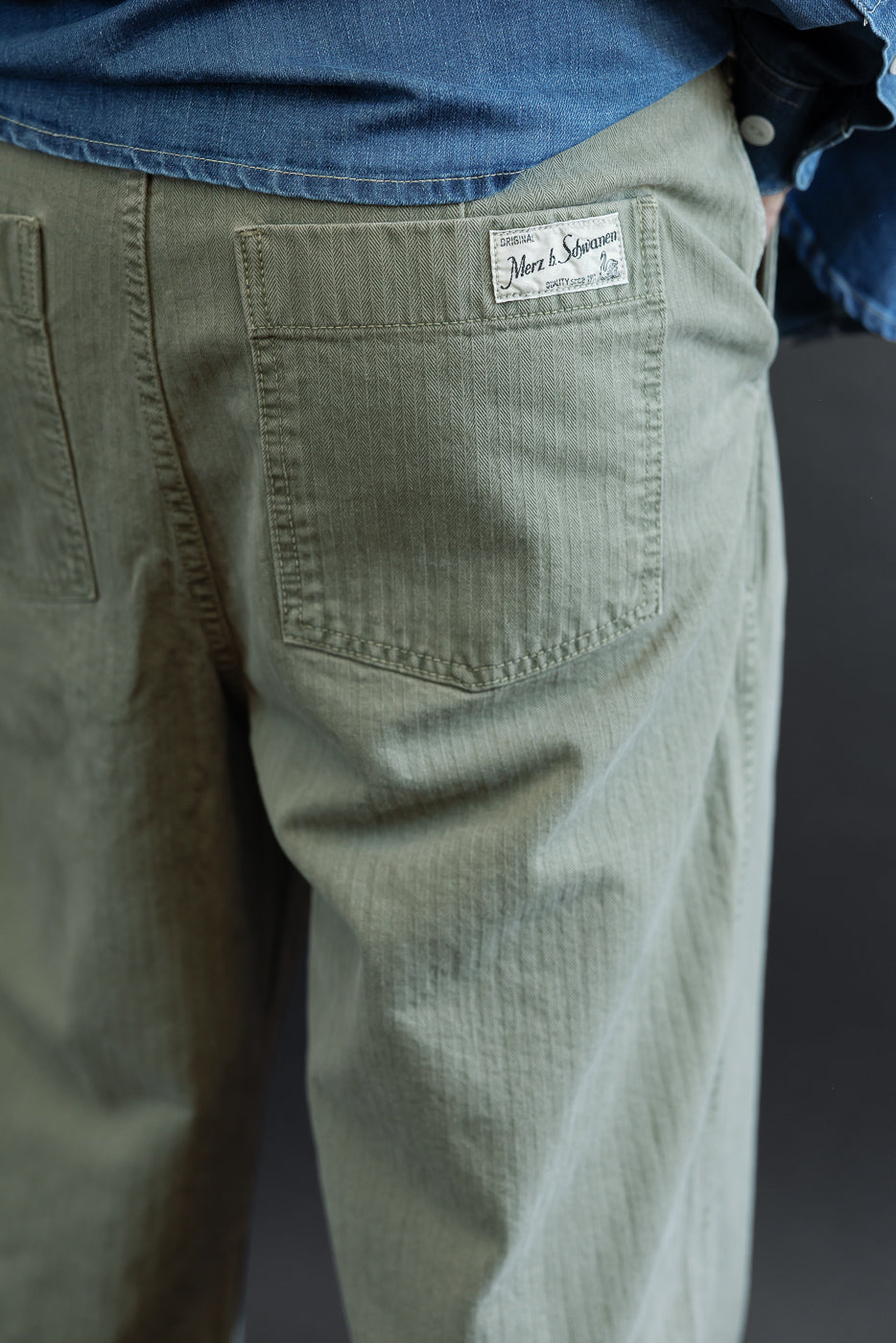 Close-up back view of olive green cotton trousers on a male model, showing rear pocket and tag.