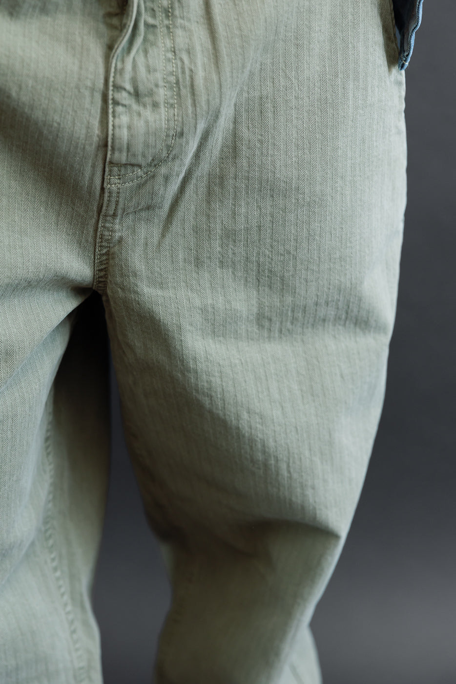 Close-up side view of sage green cotton twill fabric texture on men's casual trousers.