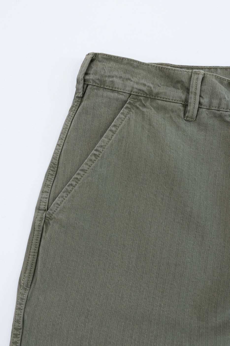 Close-up of the front left pocket and waistband of olive green twill trousers.