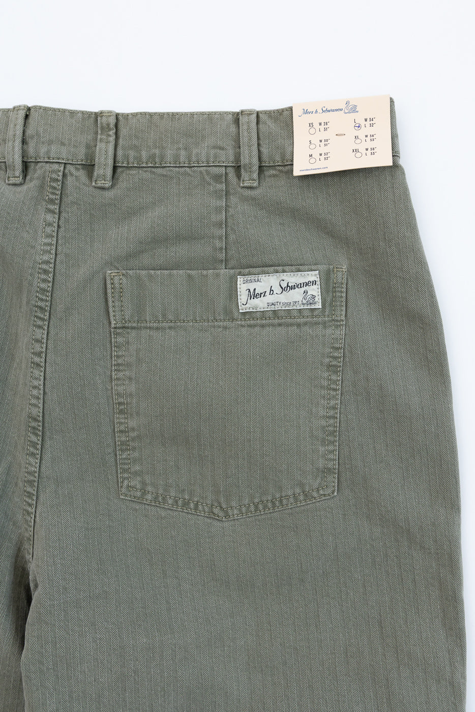 Close-up of the back of olive green trousers showing a pocket and Merz b. Schwanen tag.
