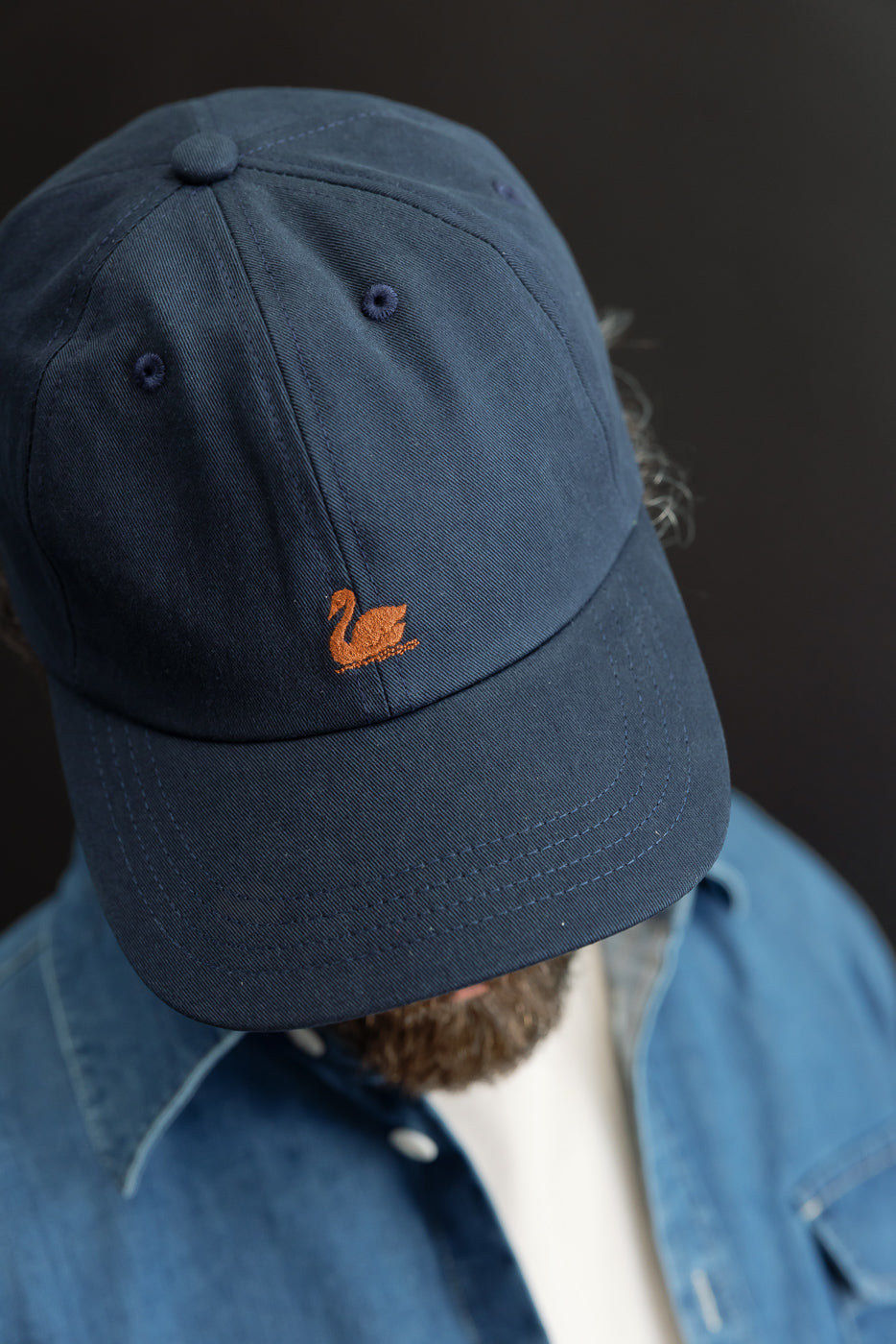 Close-up front view of a navy blue cotton baseball cap with orange swan embroidery.