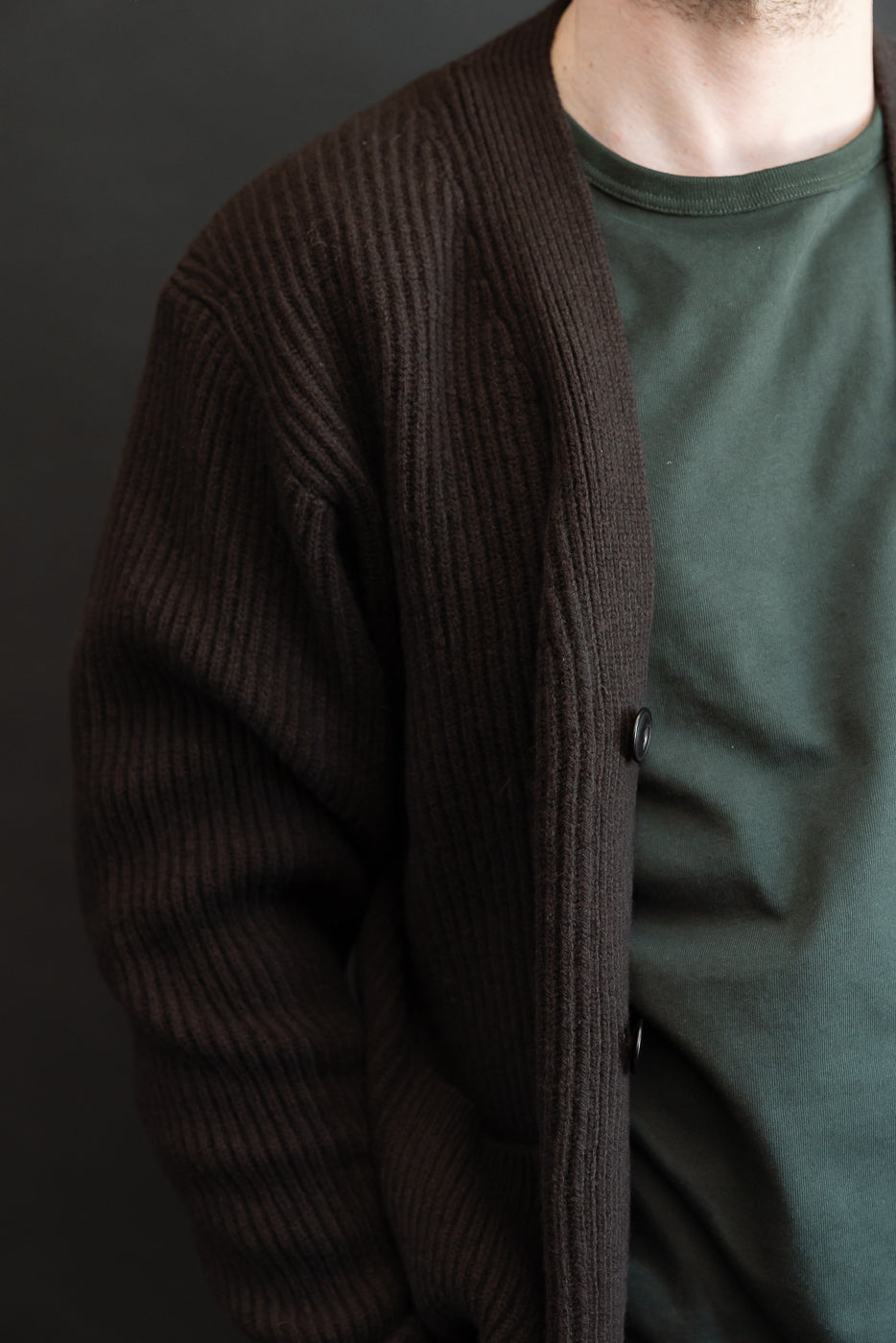 Close-up side view of a male model wearing a dark brown ribbed knit cardigan over a green tee.