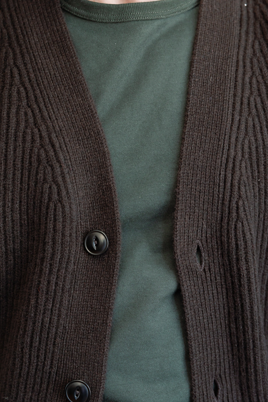 Close-up front view of a dark brown ribbed knit cardigan with black buttons over an olive green tee.