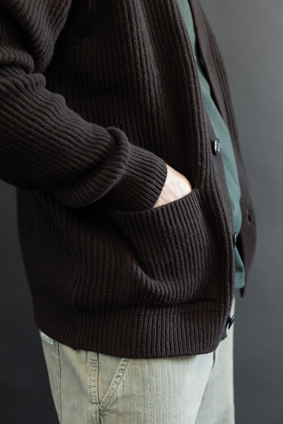 Close-up side view of a male model's dark brown ribbed knit cardigan pocket and texture.