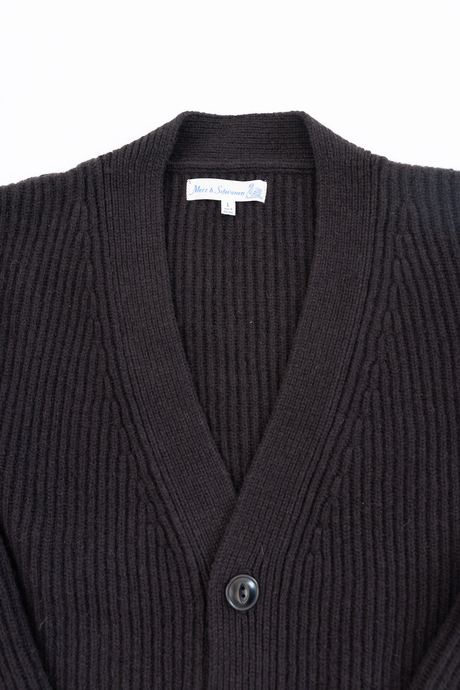 Close-up of the front of a brown ribbed cardigan featuring a Merz & Schwanen tag and button.