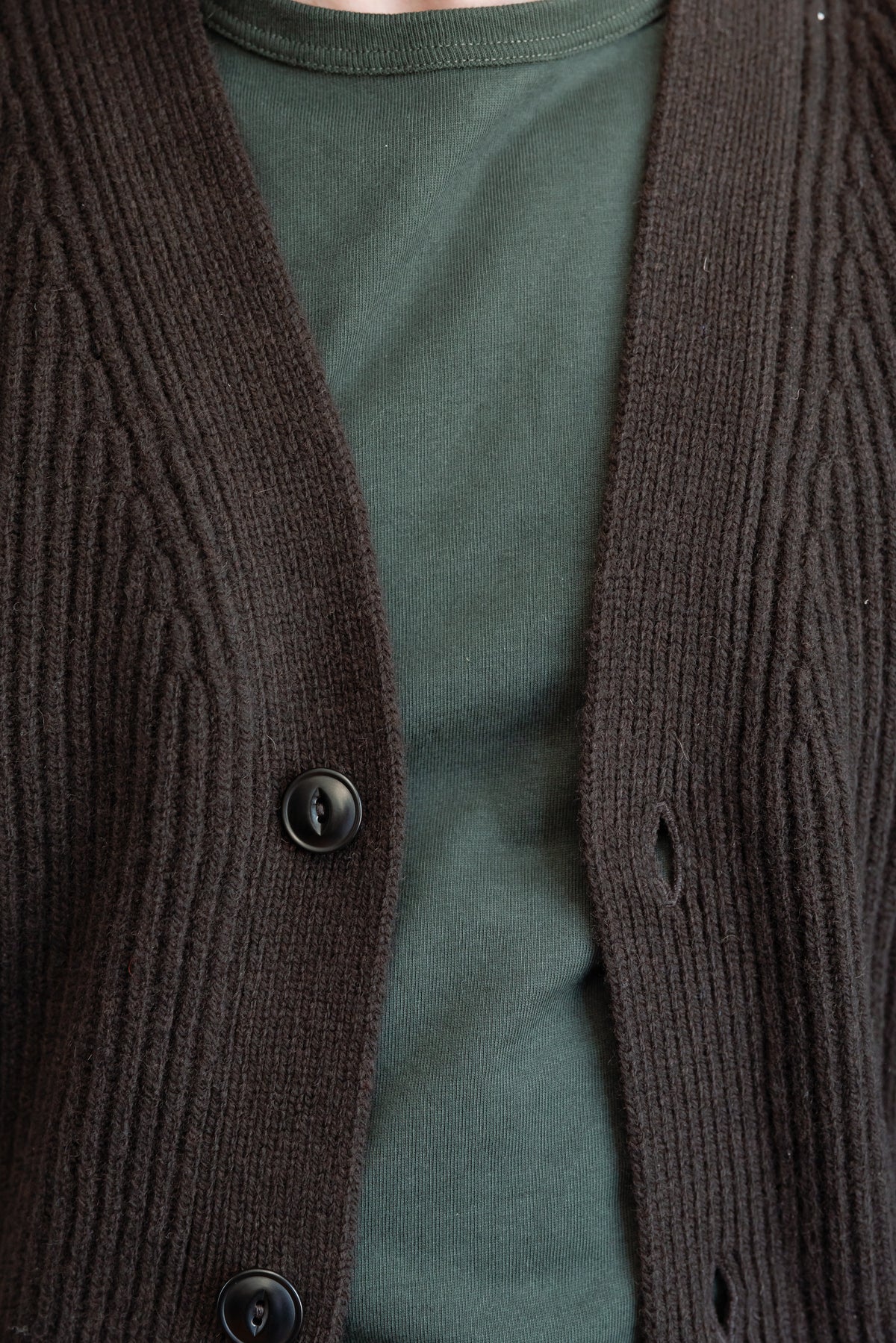 Close-up front view of a dark brown ribbed knit cardigan over an olive green t-shirt.