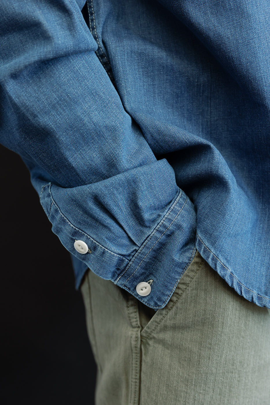 Close-up of a male model's left sleeve cuff on a blue denim shirt with white buttons.
