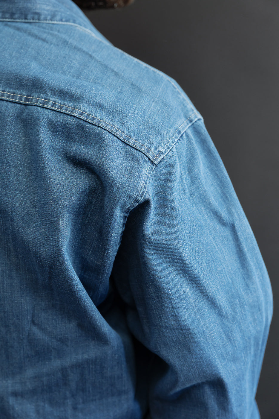 Close-up of the back shoulder and sleeve of a blue denim shirt showing fabric texture.