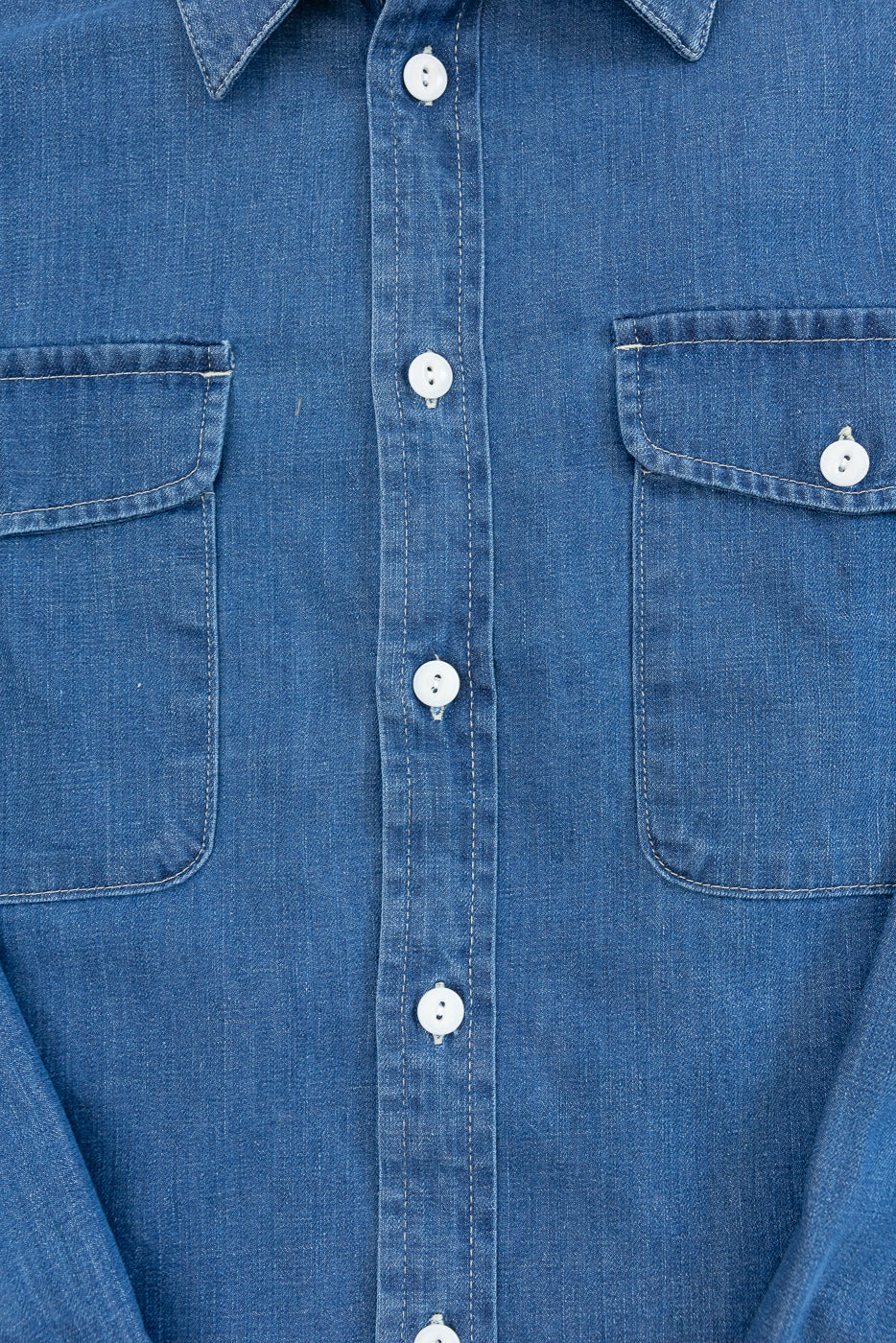Close-up front view of a blue denim shirt showing button placket and chest pockets.