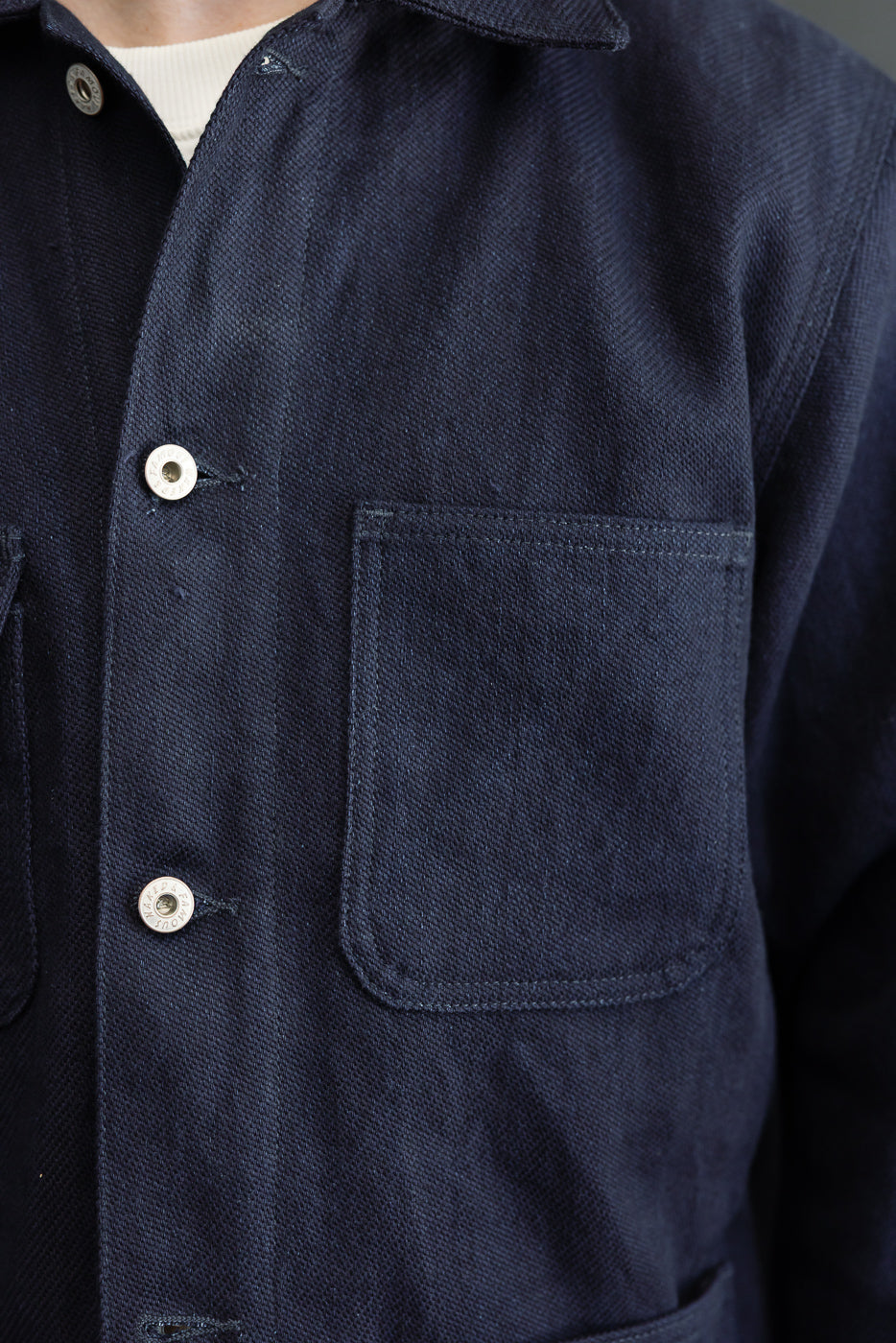 Close-up front view of navy work shirt on male model, showing button details, chest pocket, and selvedge fabric texture