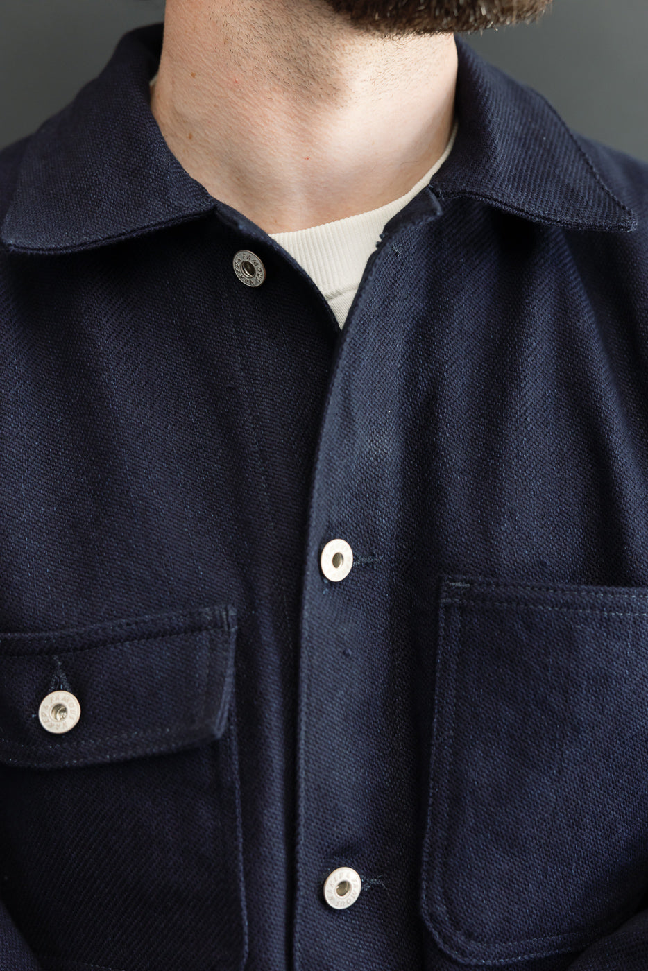 Close-up front view of navy work jacket on male model, showing collar, metal buttons, chest pockets, and textured fabric