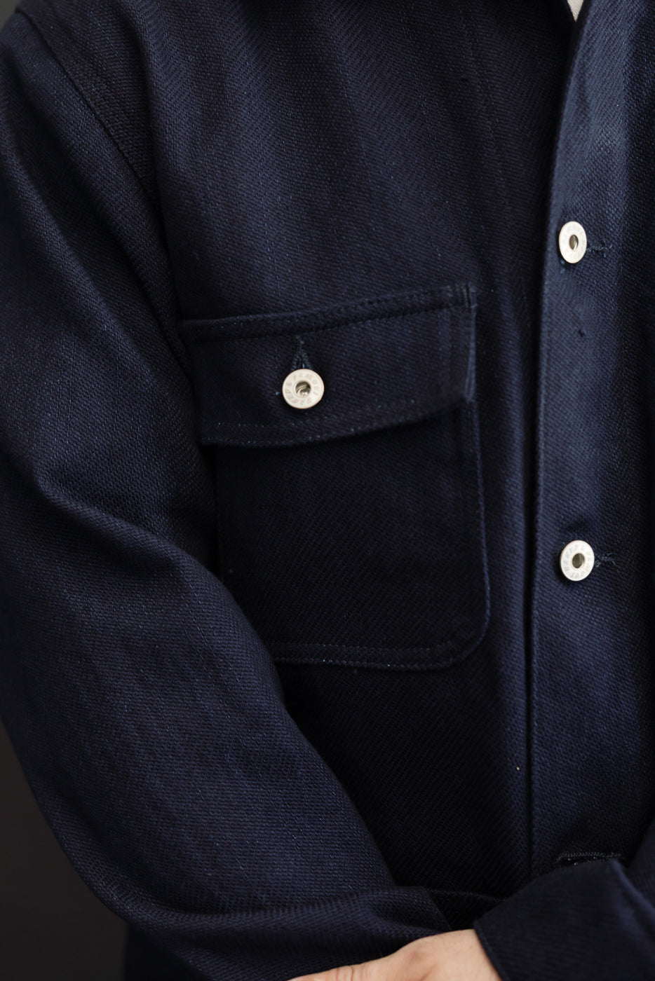 Close-up front view of navy work shirt on male model, showing chest pocket, white buttons, and textured fabric