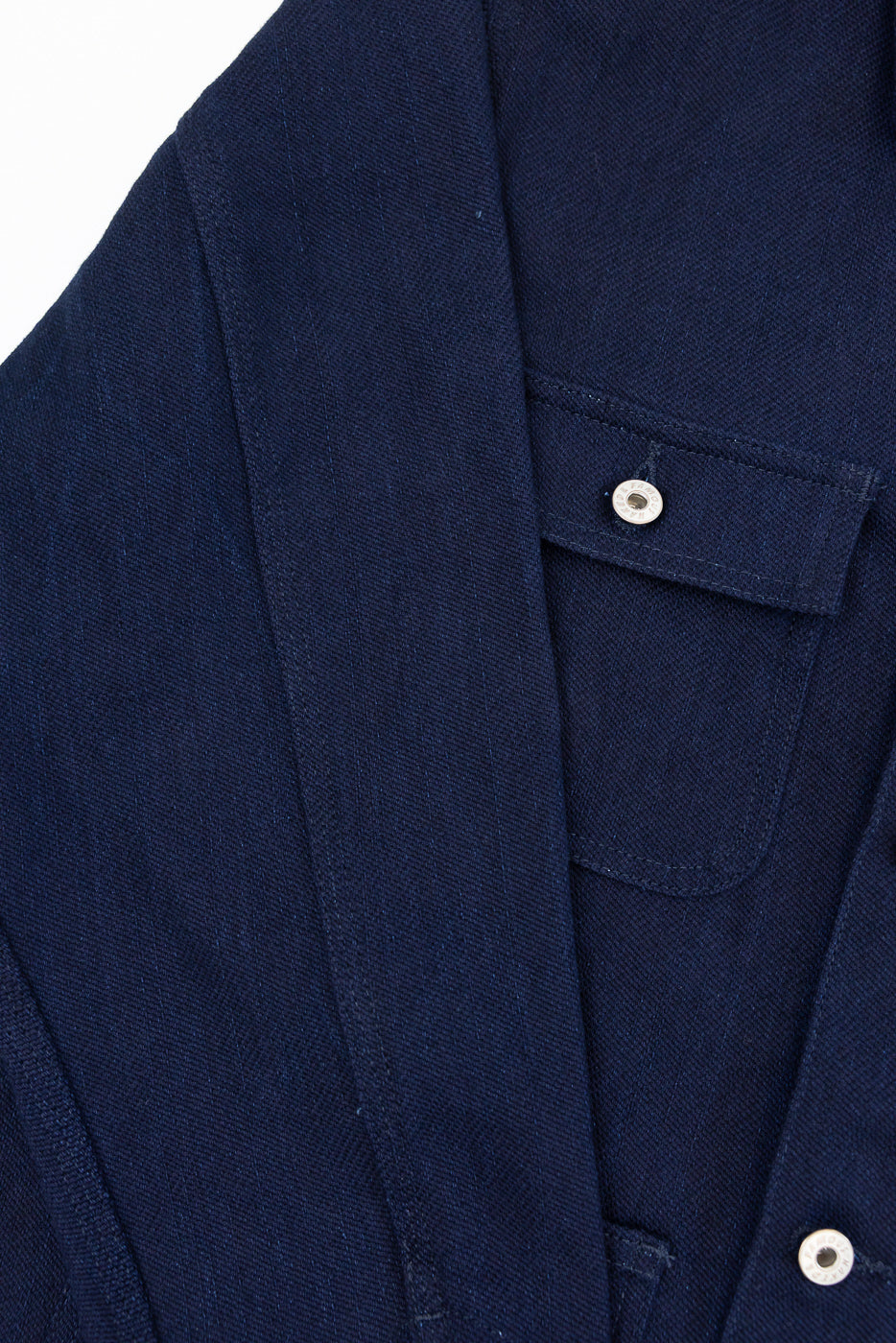 Close-up front view of navy selvedge denim shirt, showing buttoned chest pocket, silver buttons, and fabric texture