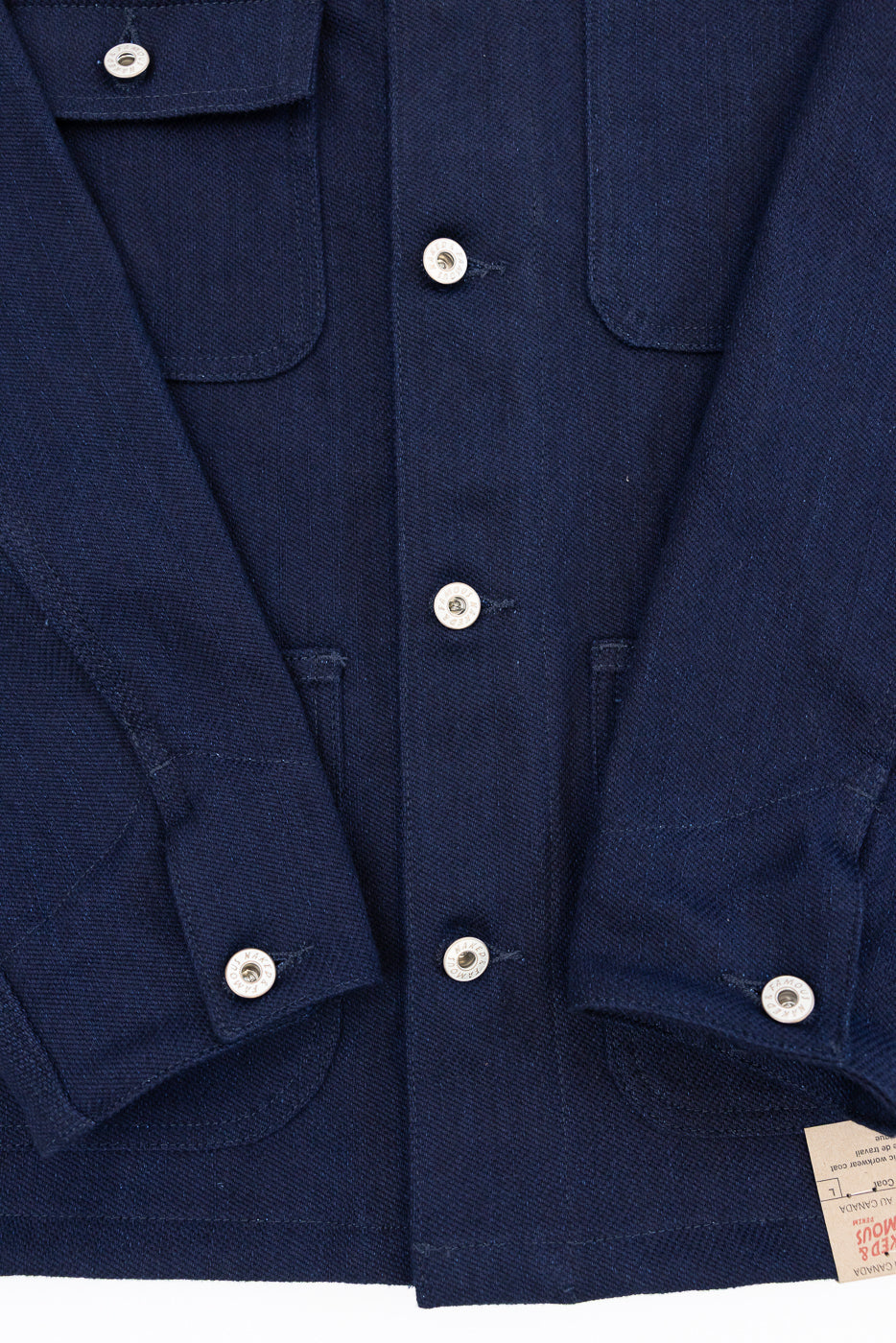 Close-up front view of navy workwear coat with silver snap buttons, chest pockets, and selvedge tag detail