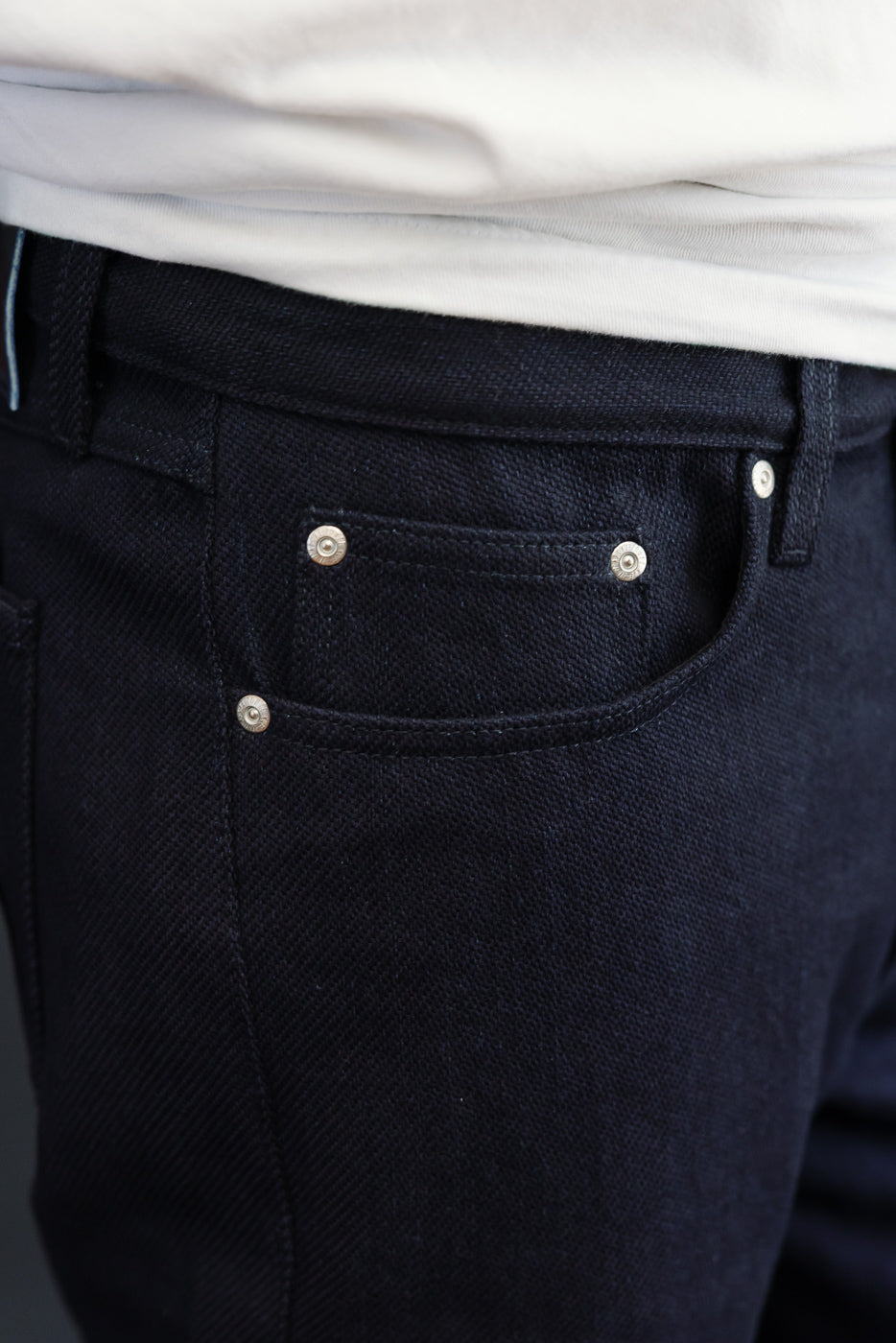 Close-up front view of dark selvedge jeans with silver rivets, worn by male model, 5'9