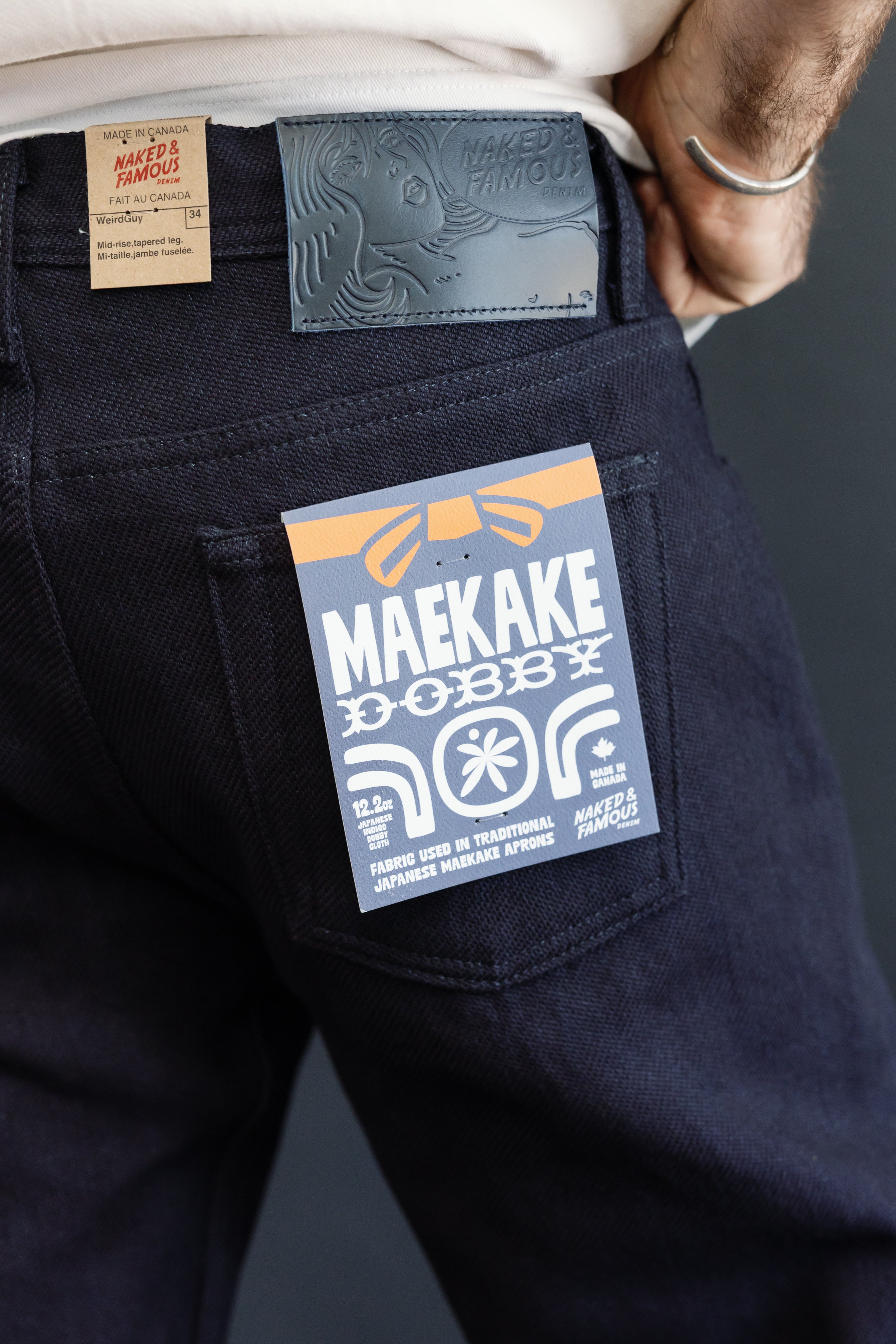 Close-up of male model's back pocket showing Maekake denim tag, leather patch, and fabric texture