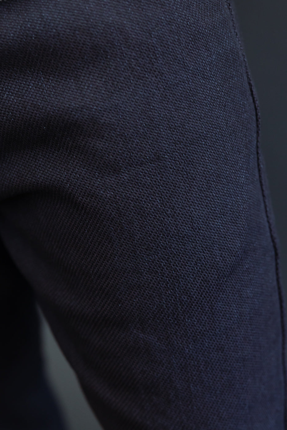 Close-up of dark navy selvedge denim fabric texture and side seam on male model's pants, showcasing detailed weave