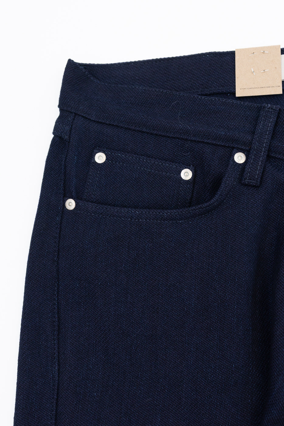 Close-up front view of dark navy selvedge jeans, showing button fly, front pocket stitching, and fabric texture.
