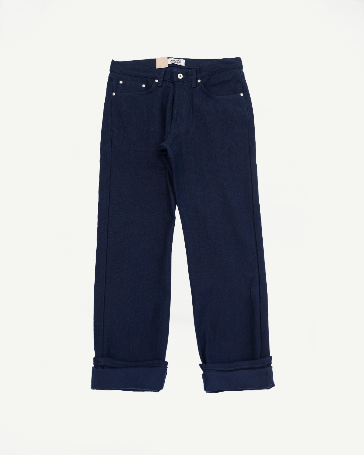 Flat lay front view of dark navy selvedge jeans with cuffed hems, button fly, and visible brand tag