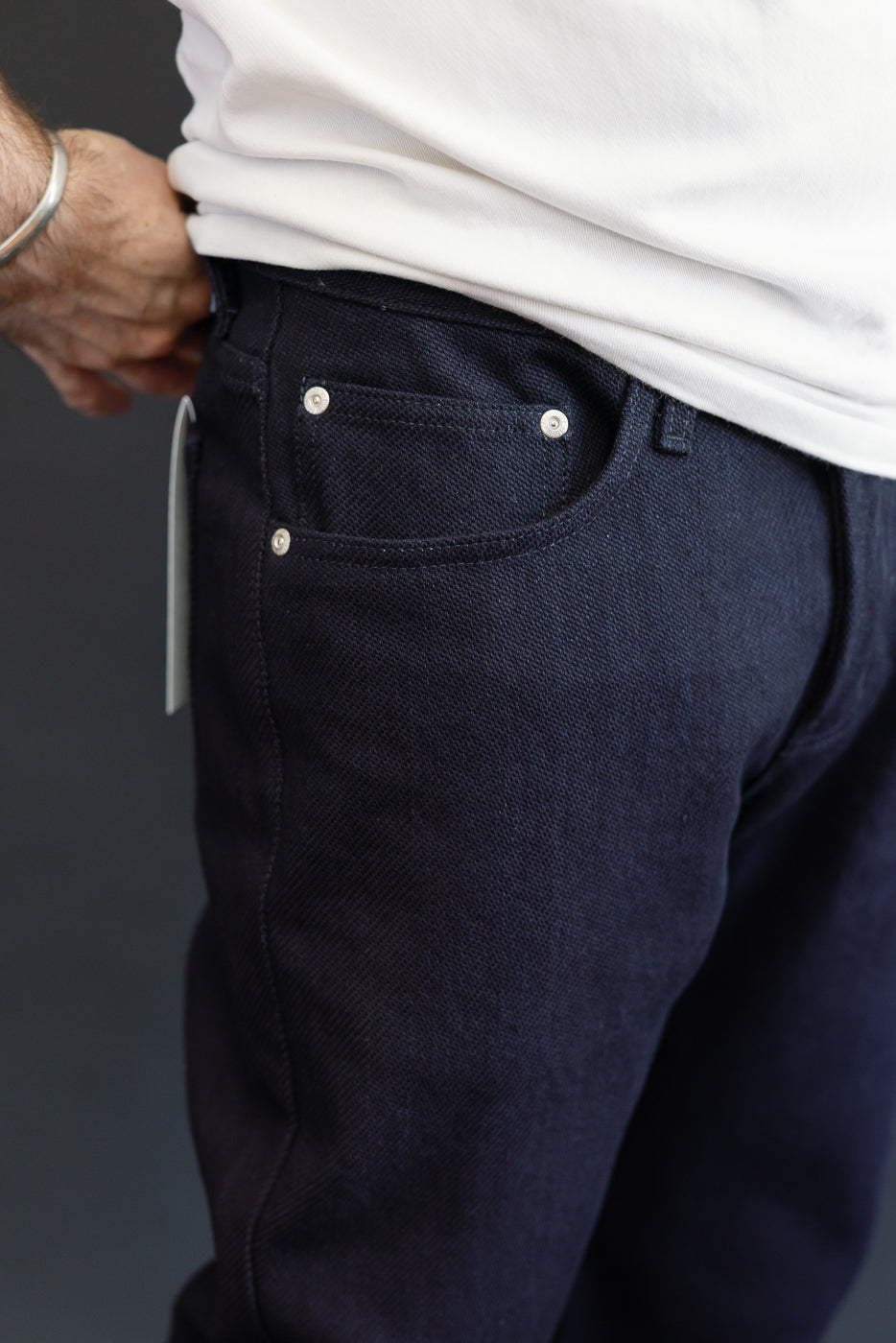 Close-up of male model's back pocket, dark selvedge jeans with silver rivets, athletic build