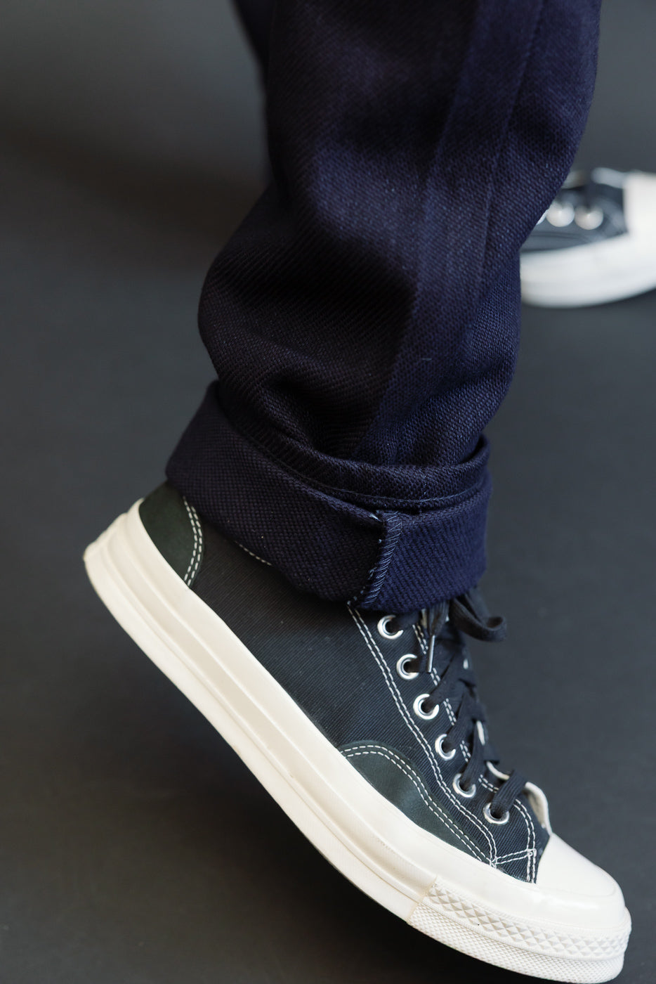 Close-up of navy selvedge jeans cuff with black sneakers, front view
