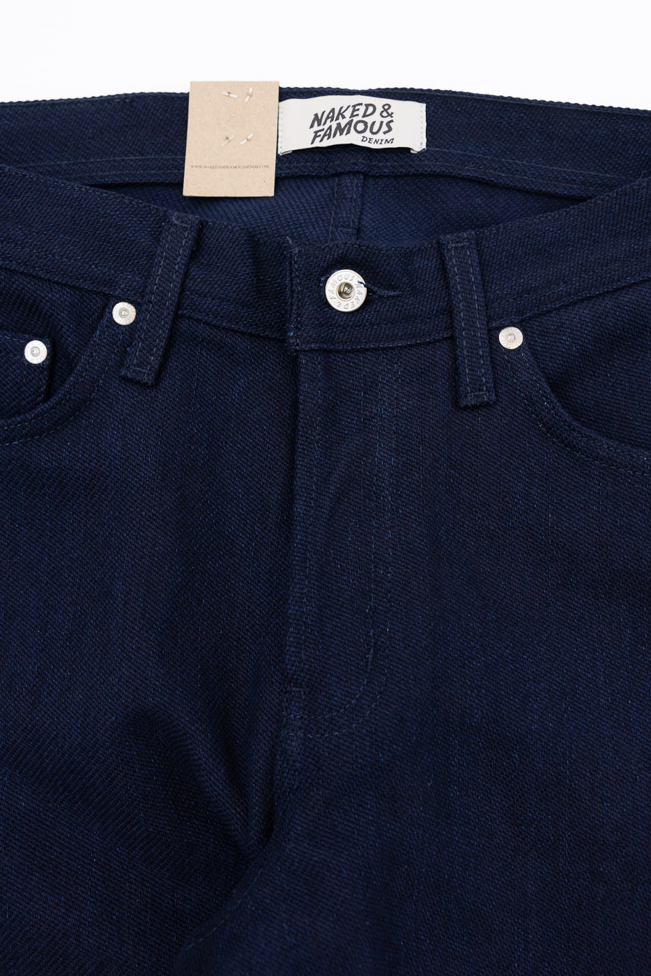 Close-up front view of dark denim jeans with button fly, metal rivets, and Naked & Famous tag