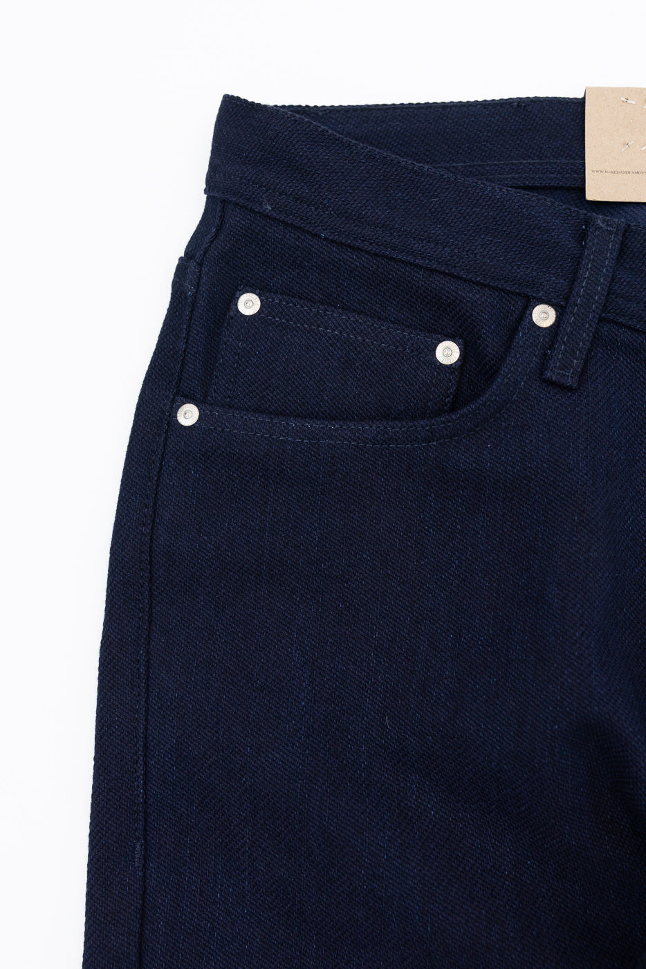 Close-up front view of dark navy selvedge denim jeans showing front pocket, silver rivets, and waistband tag detail
