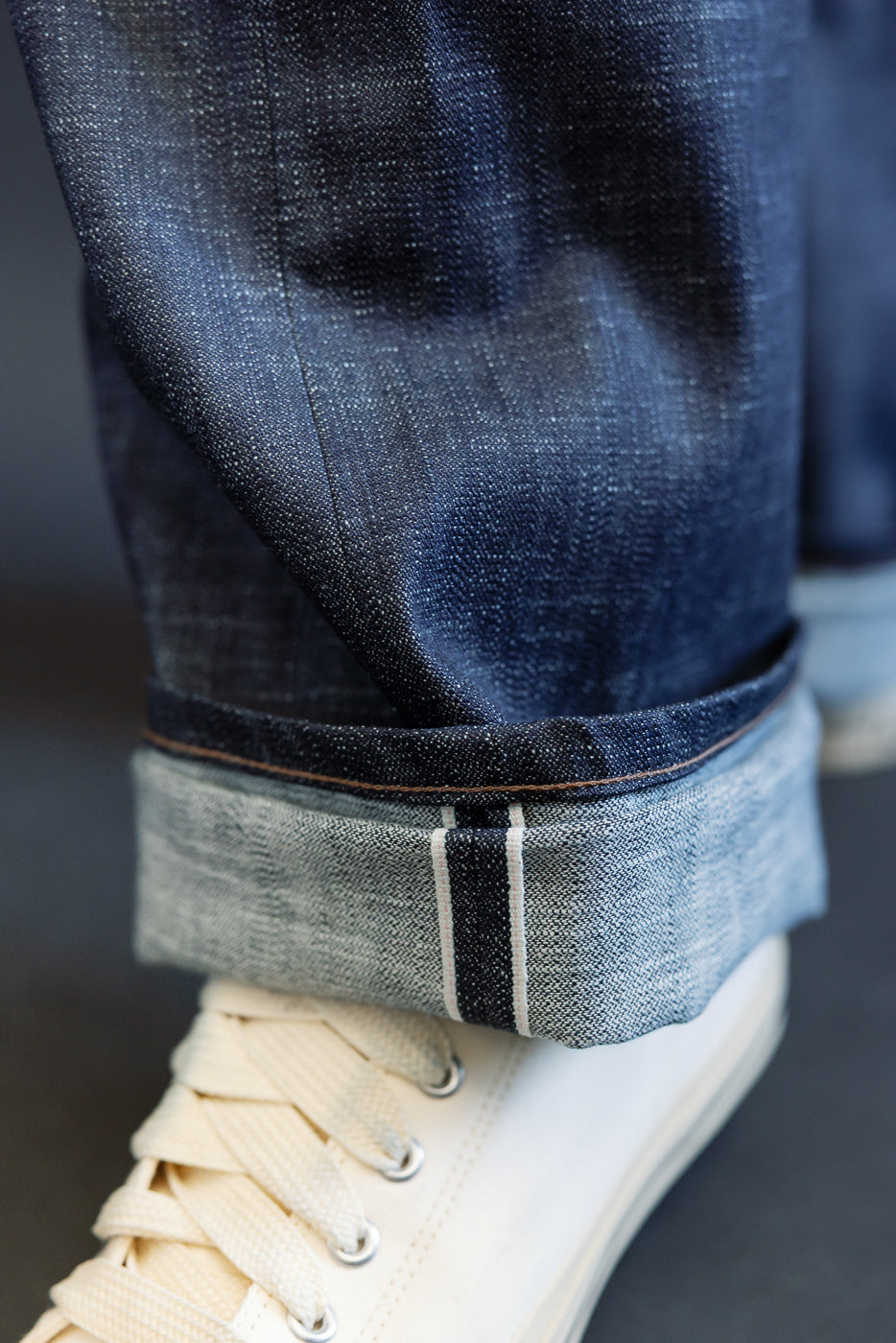 Close-up of the 12.5oz Greencast Stretch Selvedge - Strong Guy jeans, showcasing the cuffed hem with a white-and-red selvedge stripe, paired with white canvas sneakers, reflecting premium Japanese denim craftsmanship.