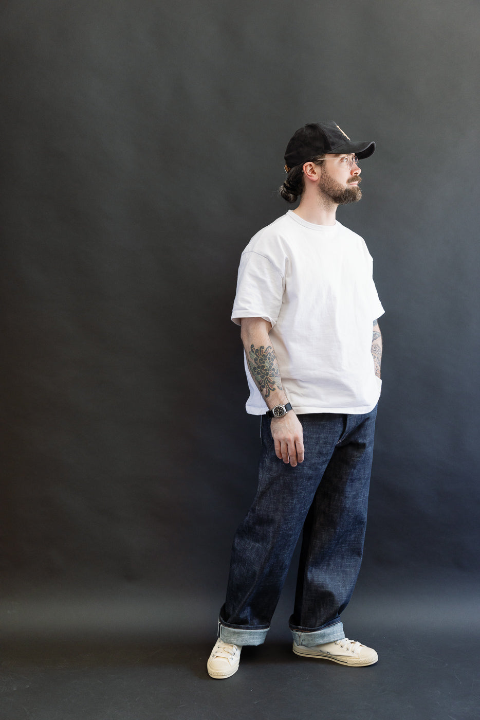 A man models the 12.5oz Greencast Stretch Selvedge - Strong Guy jeans, showcasing their relaxed fit and wide-leg design, paired with a white T-shirt and off-white sneakers, embodying Dant's premium menswear style.