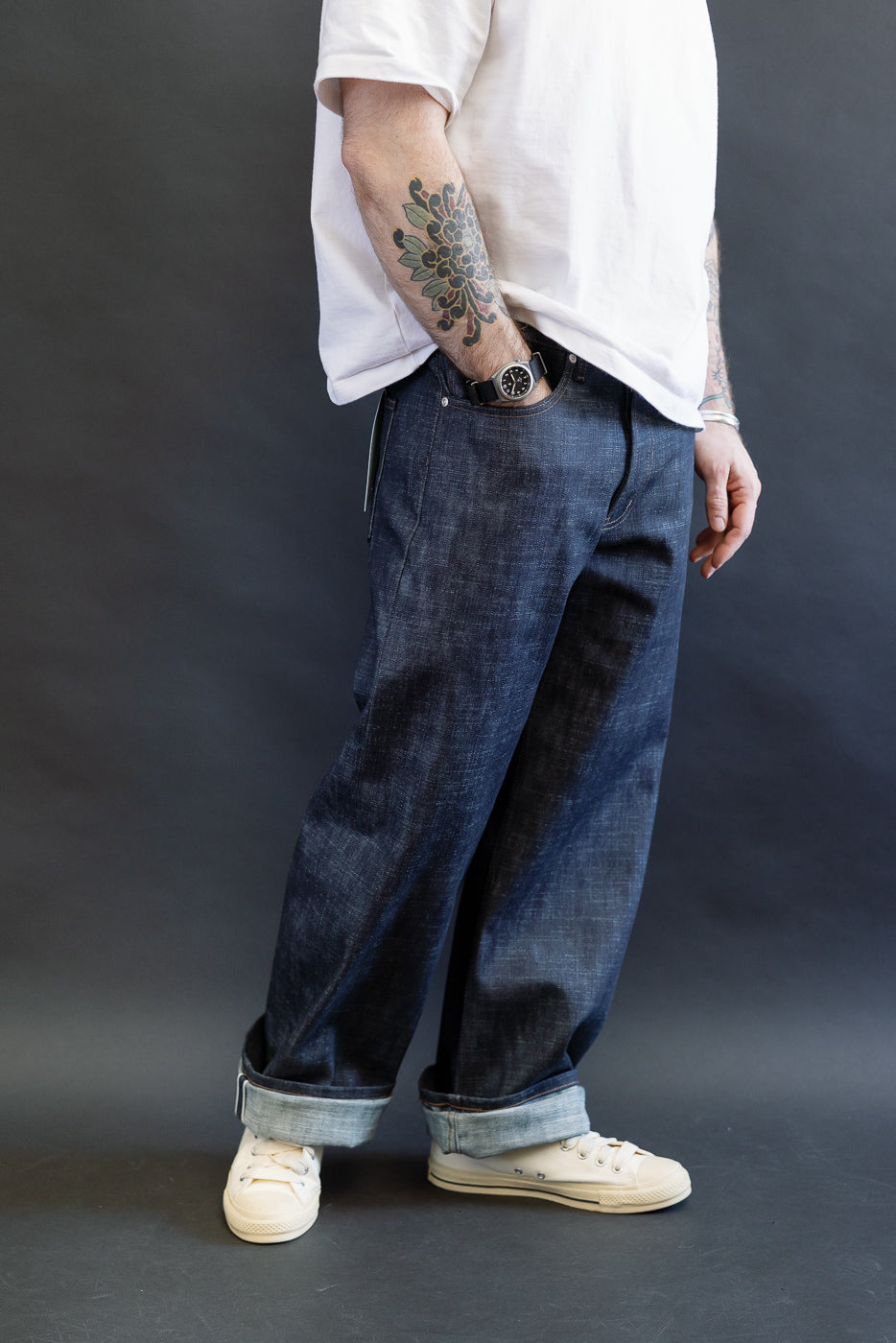 12.5oz Greencast Stretch Selvedge - Strong Guy jeans, featuring wide legs and rolled cuffs, paired with off-white sneakers and a plain white T-shirt, showcasing the denim's unique texture and fit.