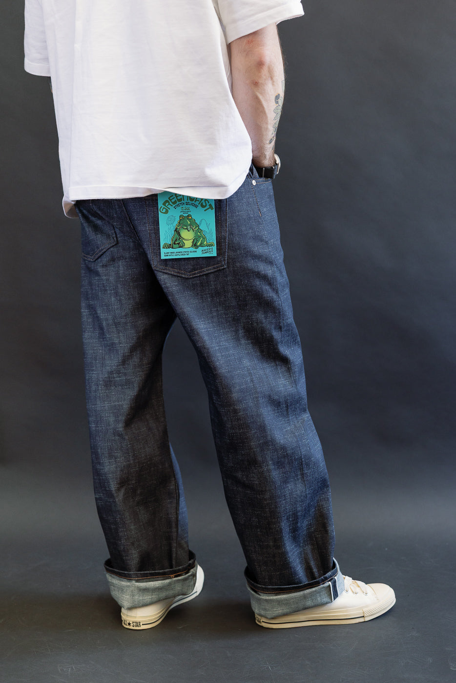 Model in white T-shirt and white sneakers showcases 12.5oz Greencast Stretch Selvedge - Strong Guy jeans, featuring a green-tagged back pocket detailing the denim's unique stretch and slub texture.
