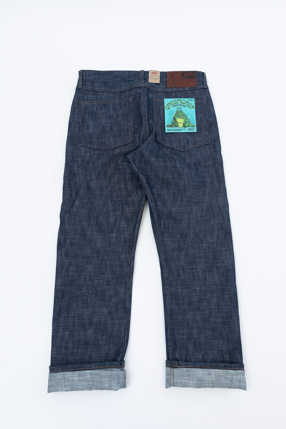 Dark-indigo 12.5oz Greencast Stretch Selvedge - True Guy jeans, back view. Features rolled hems exposing selvedge, two back pockets, leather brand patch, and GREENCAST frog label on right pocket.