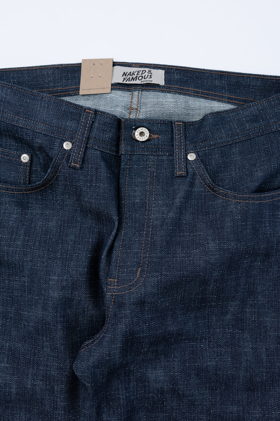 12.5oz Greencast Stretch Selvedge - Weird Guy jeans, featuring dark-indigo denim with contrast stitching, riveted pockets, and a Naked & Famous Denim label, laid flat showcasing waistband, metal button, and hang-tag.