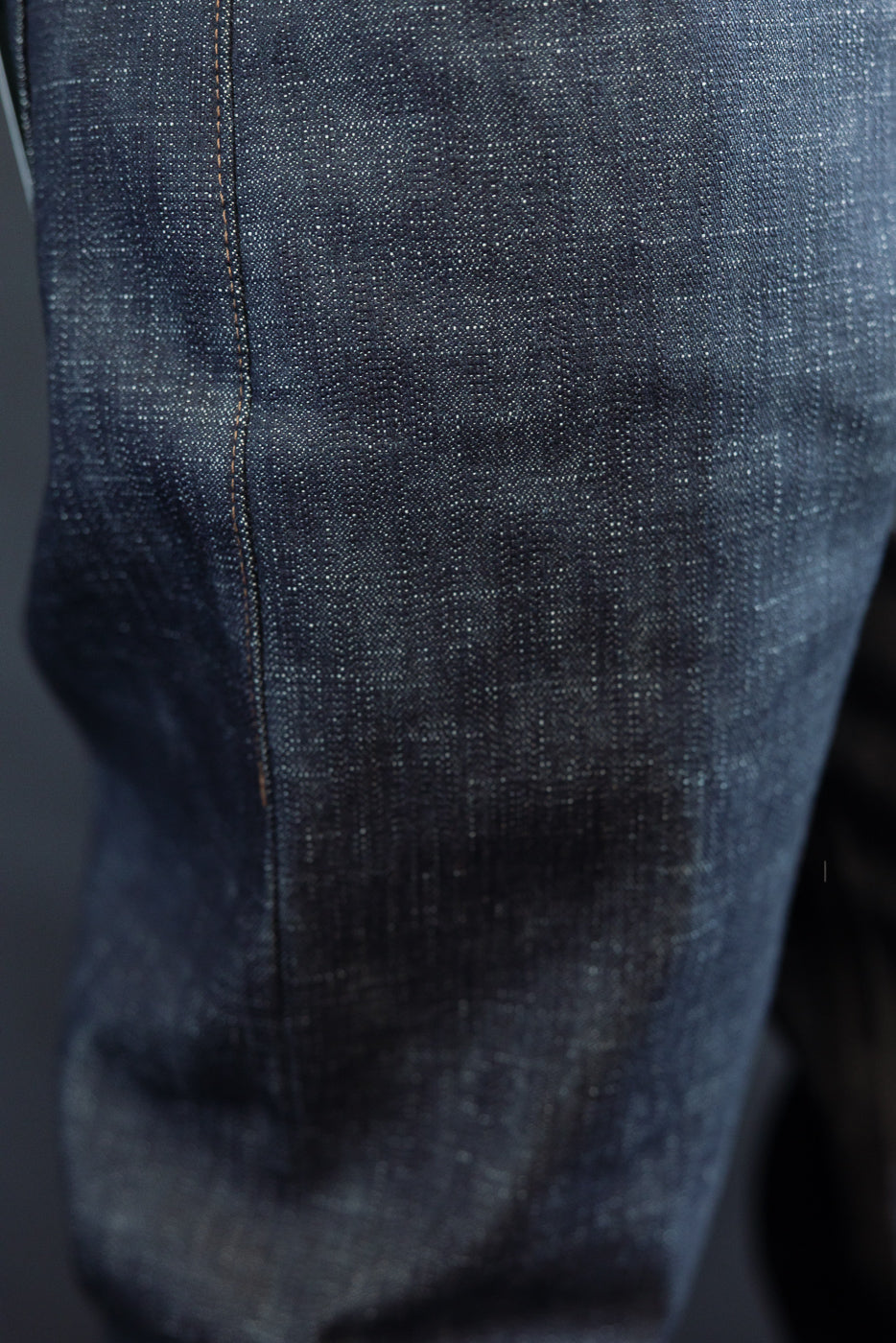 Close-up of the 12.5oz Greencast Stretch Selvedge - Weird Guy, highlighting the dark indigo denim with visible vertical seam stitching, showcasing the unique texture and subtle green cast of the fabric.